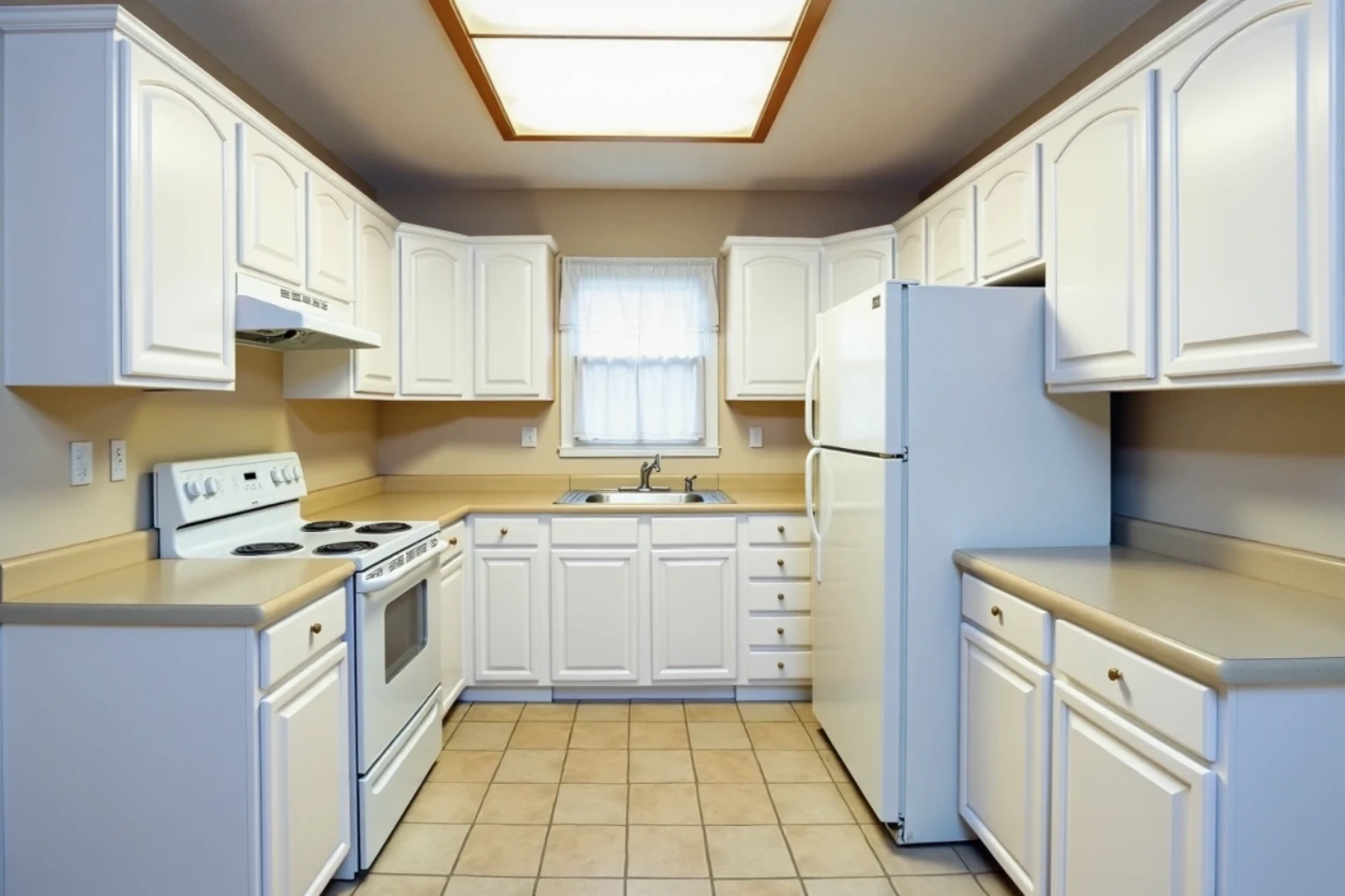 Same kitchen after refacing: white painted arched raised-panel doors and drawer fronts with small nickel knobs, counters and appliances unchanged.